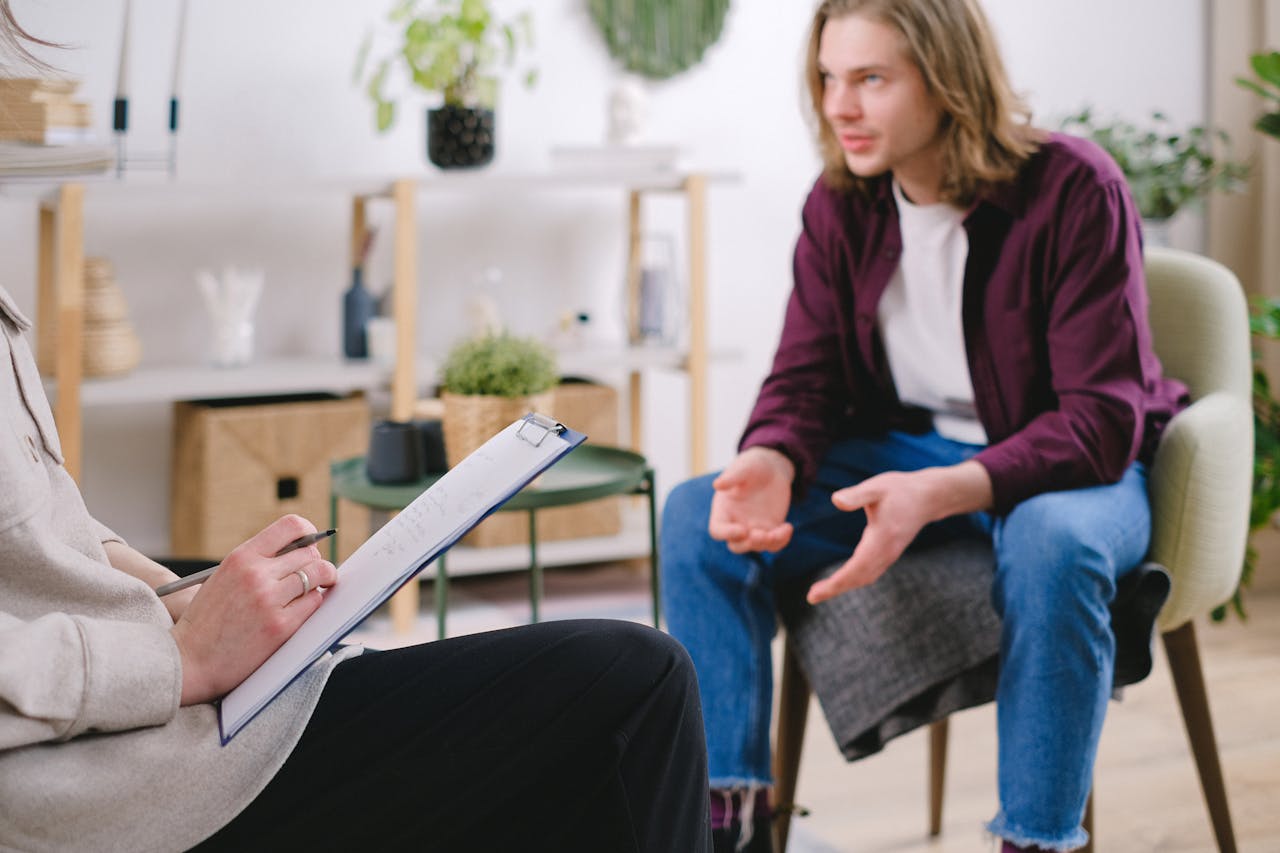 Professional therapy session with a man discussing with a therapist taking notes indoors.